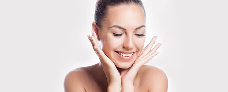 A smiling woman with bare shoulders holds both hands up beside her cheeks