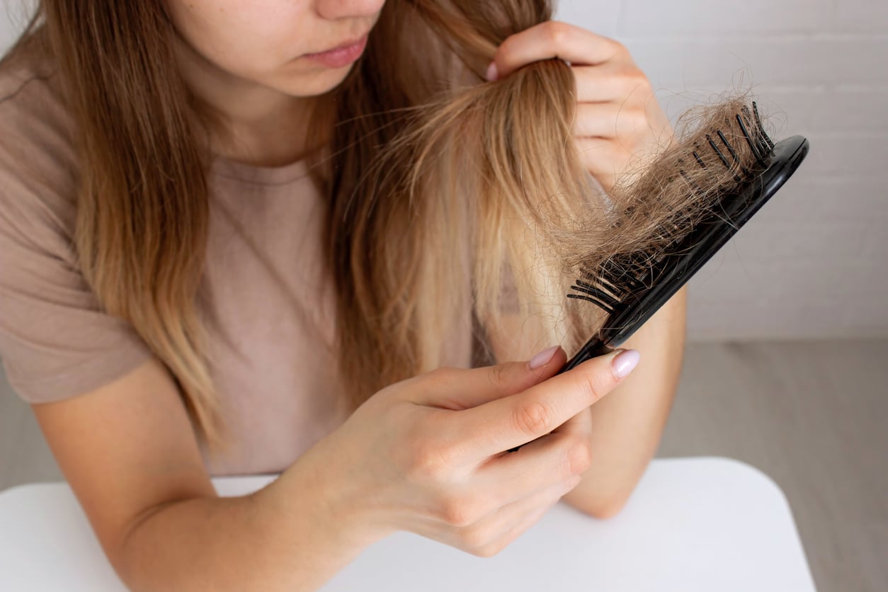 Woman examining strands of hair collected in a brush after noticing increased shedding.