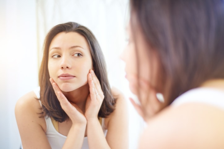 woman checking face in mirror