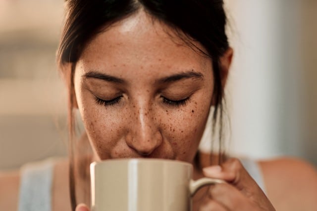 Close up of woman's face with freckles, sipping beverage out of mug