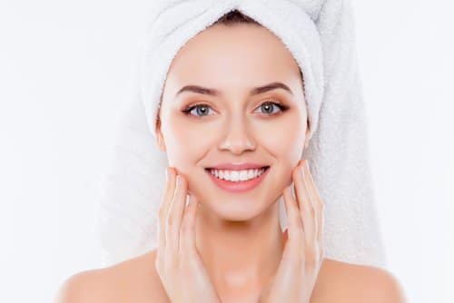 woman in towel and turban on head enjoying touching her perfect face skin with fingers