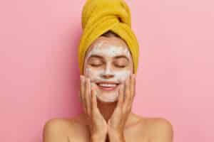 woman washes face cleans skin with soap wears yellow towel on head