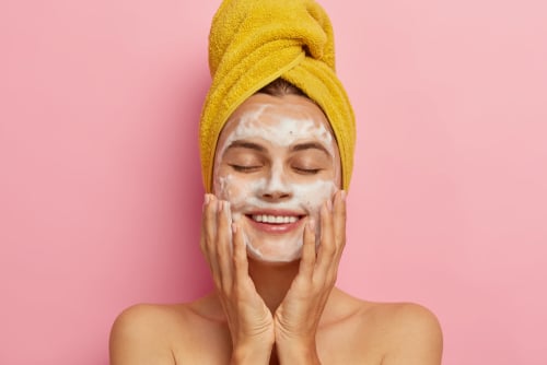 woman washes face cleans skin with soap wears yellow towel on head