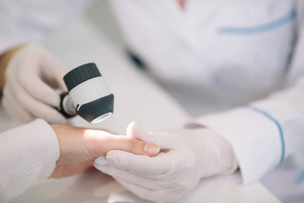 Closeup of dermatologist examining mole on hand of female patient in clinic